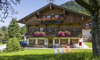 A charming wooden house with colorful flower balconies. In the foreground, there is a green lawn and lounge chairs.