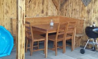 A cozy outdoor area with a wooden table and chairs. In the corner, there is a grill and a blue play area.