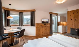 A modern studio with a double bed, a dining table, and a small kitchenette. Large windows offer a view of the surroundings.