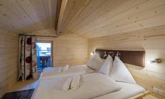 A cozy bedroom made of wood with two beds and natural materials. Large windows provide plenty of light and a view outside.