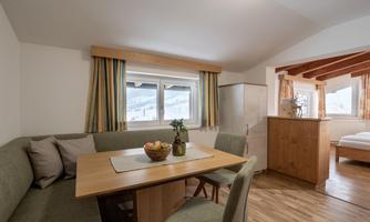 A cozy dining area with a wooden table and a seating area. Through the windows, one can see a snowy landscape.