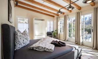 A bright bedroom with a large bed and modern furniture.  
Large windows offer views of nature and provide plenty of daylight.