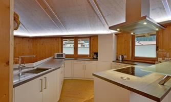 A modern kitchen with wood paneling and bright walls. It is well equipped with a cooking surface, sink, and windows that let in plenty of light.