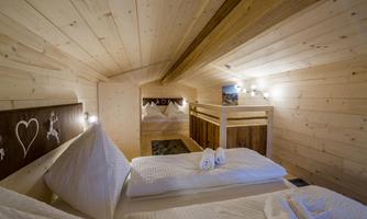 A cozy bedroom with wooden paneling and two beds. Warm light creates an inviting atmosphere.