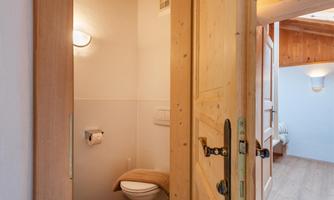 A modern bathroom with a wooden-type door. The wall is bright and the lighting is pleasant.