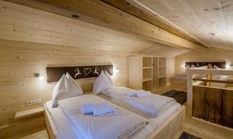 A cozy bedroom with a wooden ceiling and two beds. The atmosphere is warm and inviting, ideal for a relaxing holiday.