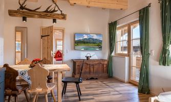 A cozy living kitchen with wooden furniture and large windows. The room is bright and inviting, with a TV and a view of the countryside.
