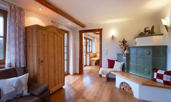 A cozy living space with wooden paneling and a tiled stove. Bright walls and a warm wooden floor create an inviting atmosphere.