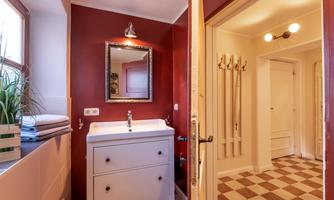 A modern bathroom with red wall color and a white sink. The room is bright and well-lit, featuring a large mirror and a warm, inviting atmosphere.