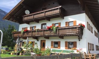 A beautiful old wooden house with blooming balconies and a well-kept garden. The surroundings are surrounded by mountains.