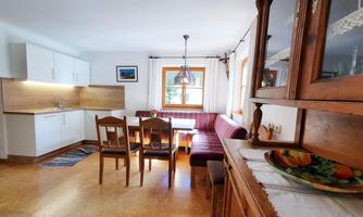 A cozy kitchen with a dining table and a seating area. The decor is bright and friendly with wooden details.