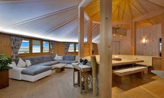 A modern living space with wooden paneling and large windows. The room is cozily furnished with a comfortable sofa and a dining area.