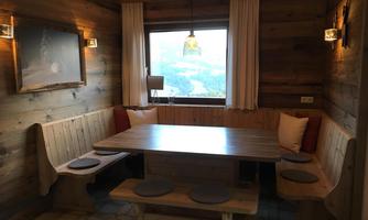 A cozy dining area made of wood with a large table and bench set. Large windows let in plenty of light and offer a view of the landscape.