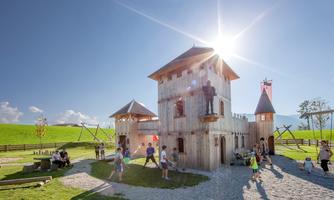 A playground with a wooden castle, surrounded by green meadows. Children are playing and having fun in sunny weather.