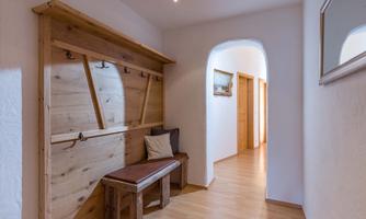 A bright hallway with a wooden bench and a coat rack on the wall. In the background, additional doors and a mirror are visible.
