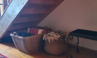 A cozy room under a staircase with two woven baskets and a small table. The floor is made of wood and a redesigned carpet lies underneath.