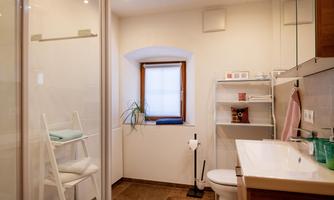 A modern bathroom with a shower and large windows. There is a sink area and shelves for towels.