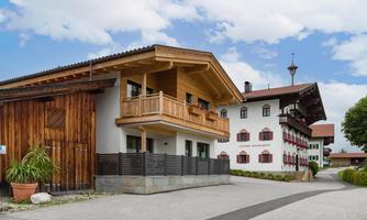 A traditional Bavarian building with a wooden facade and balcony. Next to it is another rustic house in a quiet, rural setting.