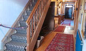 A tasteful hallway with a wooden staircase and colorful carpets. In the background, there are more rooms and a friendly lighting.