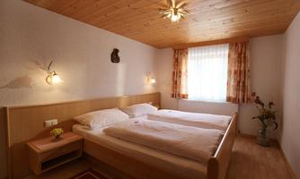 A cozy bedroom with two single beds and wooden wall paneling. The windows let in plenty of light and create an inviting atmosphere.