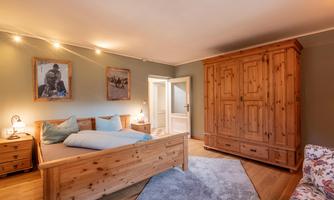 A cozy bedroom with a wooden bed and a large wardrobe. The walls are painted in soft tones and decorated with pictures.