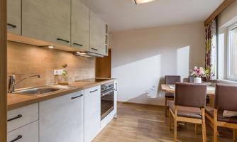 A modern kitchen with wooden flooring and clean lines. The dining area is furnished with a table and chairs and has plenty of natural light.