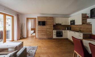 A modern kitchen with wooden cabinets and light walls. The living area is open-plan with a cozy sofa and dining space.