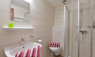 A modern bathroom with a shower, sink, and toilet. The white tiles create a bright and clean atmosphere.
