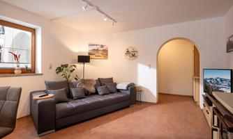 A modern living room with a gray sofa and a floor lamp. A window provides natural light and the room has a warm, inviting tone.