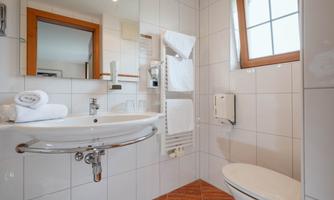 A modern bathroom with white tiles and bright colors. It includes a sink, a toilet, and a towel holder.