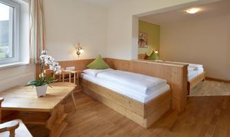 The bedroom is equipped with a double bed, a single bed, and a TV. There is direct access to a small balcony from the room.