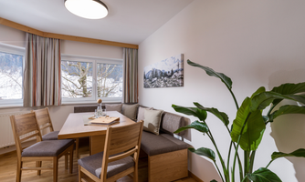A cozy dining area with a wooden chair and a large table. Large windows let in plenty of light and offer a view of the nature outside.