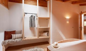 A bright, modern room with a wooden ceiling and warm light. There is a cozy seating area as well as shelves with clothing.