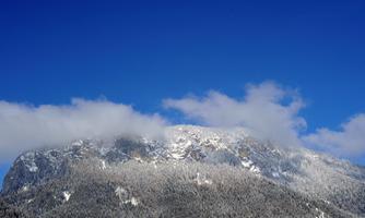 An impressive mountain with snow-covered slopes and a clear blue sky. White clouds gently drift above.