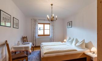 A cozy bedroom with two beds and a small table. Bright walls and a window create a friendly atmosphere.