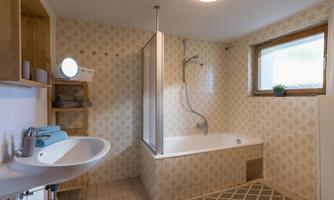 A modern bathroom with a bathtub and separate shower. The walls are decorated with a light pattern, and a window provides natural light.