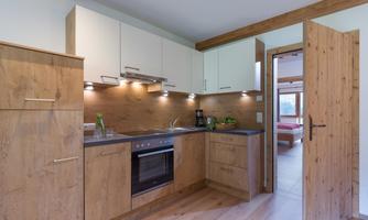 A modern kitchen with wooden furniture and an elegant design. The room is bright and inviting, with an open door to the living room.