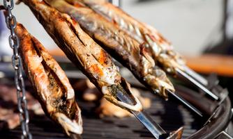 Grilled fish are hanging on skewers over the grill. They are golden brown and look delicious.
