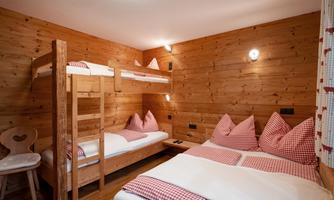 A cozy room with wooden cladding and a bunk bed. There are several beds with checked pillows and blankets.