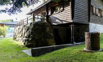 A cozy wooden house with a solid stone foundation. The garden is green and well-kept, surrounded by trees.