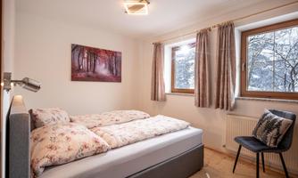 A cozy bedroom with a bed and floral bedding. Two windows offer a view of a snowy landscape.
