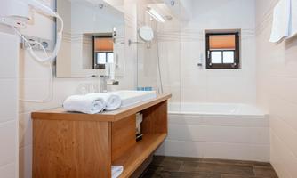 A modern bathroom with a bathtub and a wooden shelf. Clean towels and a sink are also visible.
