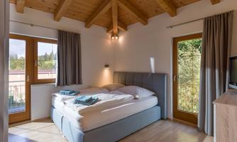 A cozy bedroom with a wooden ceiling and large windows. The bed is comfortable and tidy, ideal for a relaxing night.