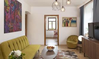 A modern living room with a green sofa and a round table. Colorful pictures hang on the walls and there is pleasant lighting.