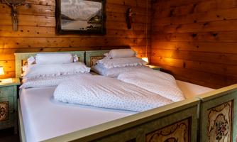 A cozy bedroom with a double bed and wooden paneling. On the wall hangs a painting depicting a rural landscape.