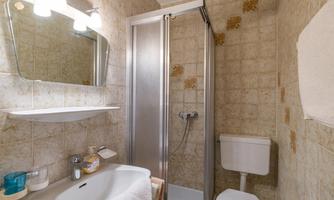 A small bathroom with a shower, a sink, and a toilet. The walls are light and decorated with tiles.