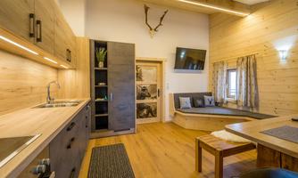 A modern kitchen with wooden surfaces and a cozy seating area. Large windows ensure plenty of daylight and a pleasant atmosphere.