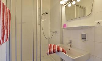 A modern bathroom with a shower and a sink. Towels with red stripes are hanging on the wall.