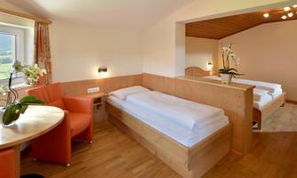 A bright room with two single beds and modern wood design. There is a small table with orange chairs and a plant as decoration.