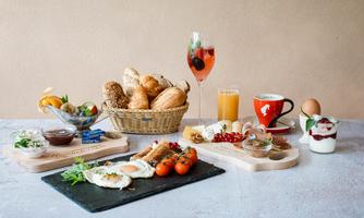 A rich breakfast buffet with various rolls, eggs, tomatoes, and a selection of drinks. In addition, fresh fruit and sweet spreads.